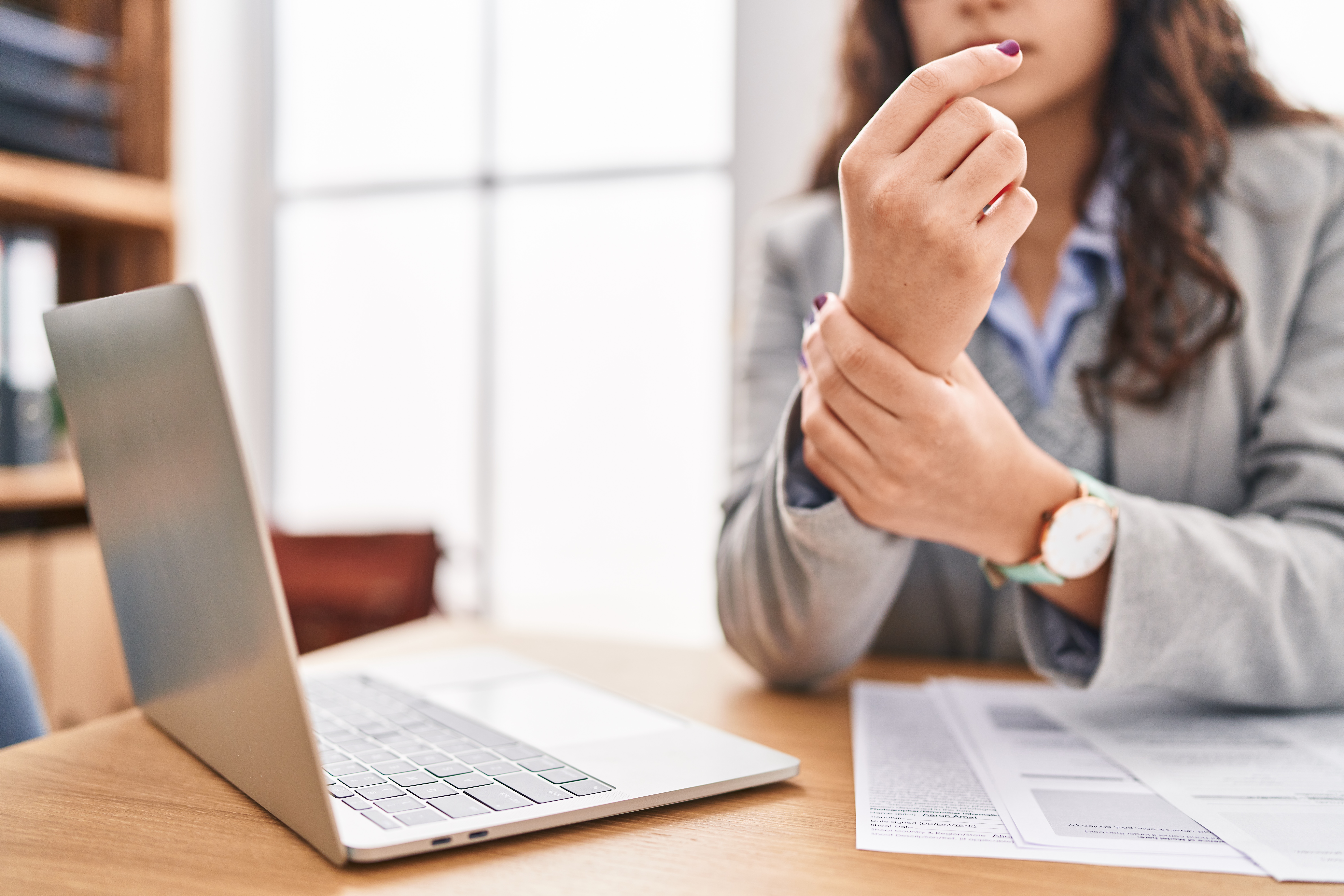 Person holding their wrist in discomfort at a laptop